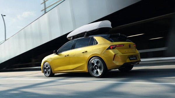 Yellow car with a roof box driving in an urban environment.